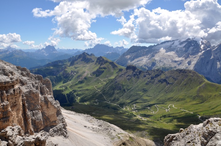 Green valley and jagged Dolomite peaks under summer clouds.