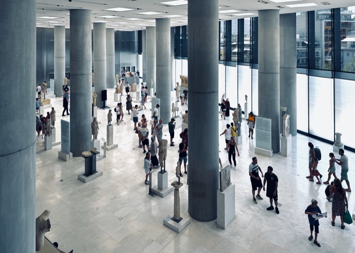 Bright museum hall with columns, statues and visitors.